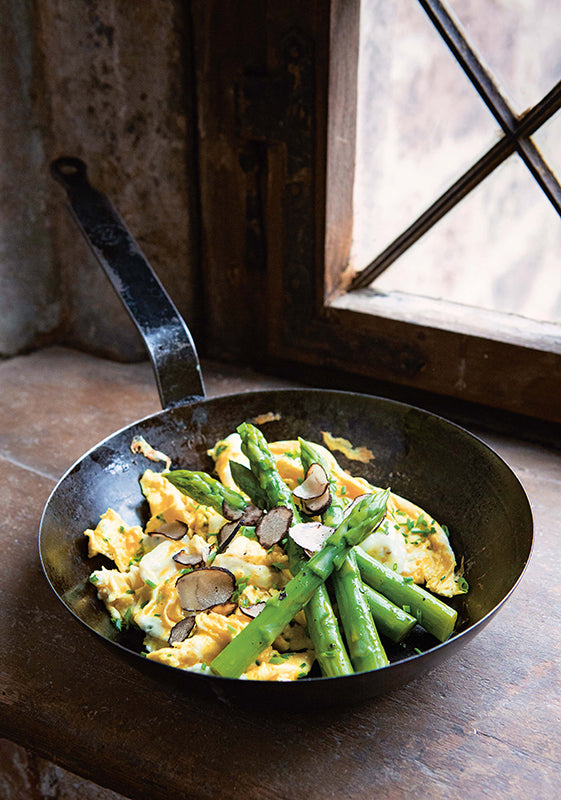 Pfanne mit grünem Spargel, cremigem Rührei und frisch gehobeltem Trüffel – servierfertiges Frühlingsgericht auf rustikalem Fensterbrett.