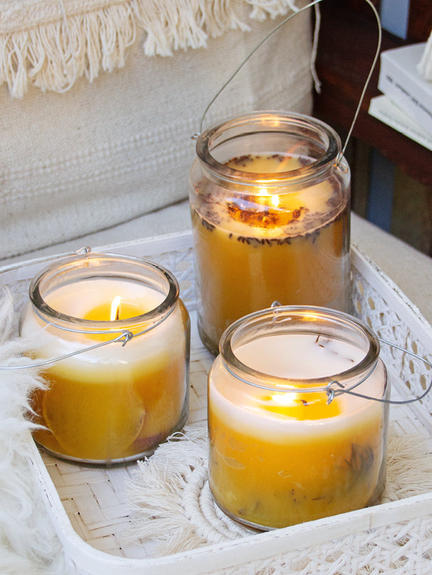 Drei handgemachte Duftkerzen im Glas mit Henkel aus Bienenwachs, dekoriert mit Kräutern und Orangenscheiben