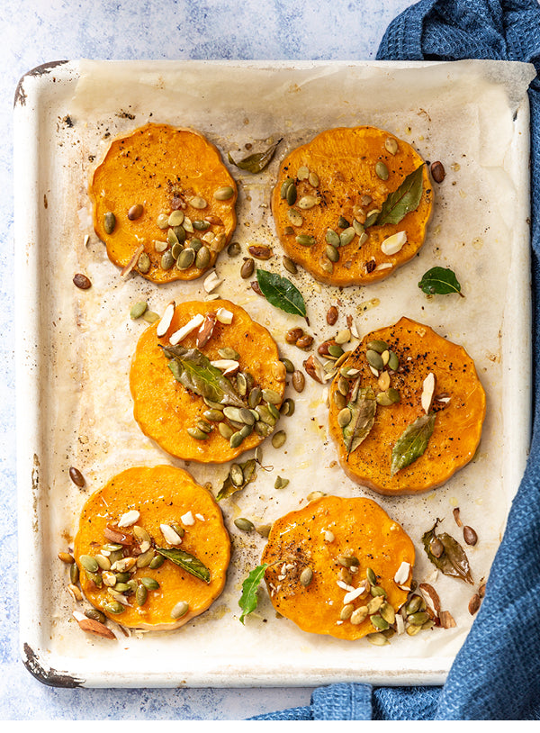 Gerösteter Ofenkürbis mit Kräutern, Kernen und Salzmandeln auf einem Backblech – goldbraun gebacken, aromatisch und herbstlich angerichtet.