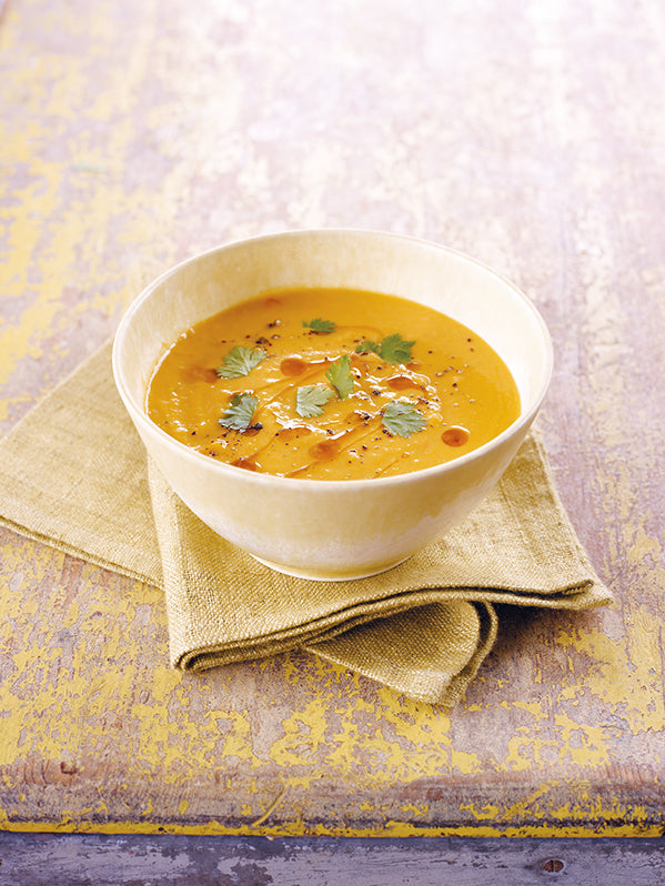 Cremige Kürbissuppe mit Kokosmilch, garniert mit frischem Koriander und Sesamöl, serviert in einer hellen Schale auf einem Leinentuch.