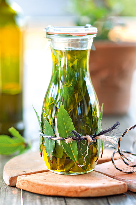 Selbstgemachtes Basilikum-Lorbeer-Öl in dekorativer Flasche mit Knoblauch und Lorbeerblättern – mediterranes Kräuteröl für Salate, Pasta und mehr