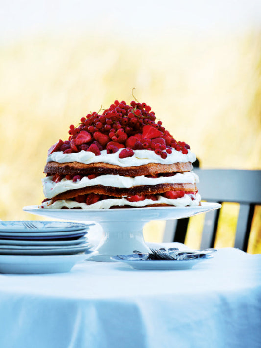 Sommerliche Schichttorte mit frischer Vanillecreme und gemischten Beeren auf einer Tortenplatte im Freien serviert
