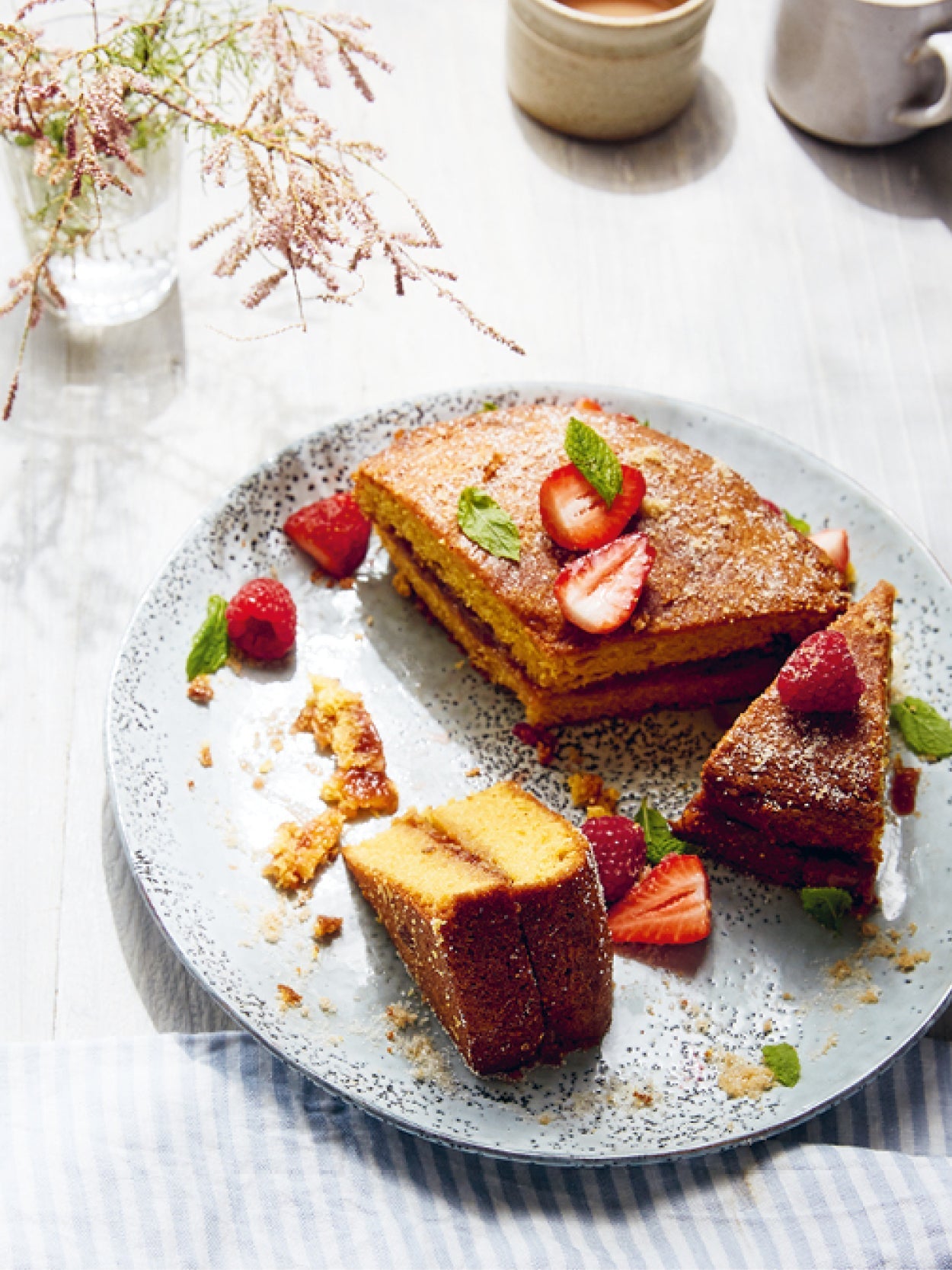 Hausgemachter Biskuitkuchen mit frischen Erdbeeren und Himbeeren, garniert mit Minzblättern auf einer rustikalen Keramikplatte serviert