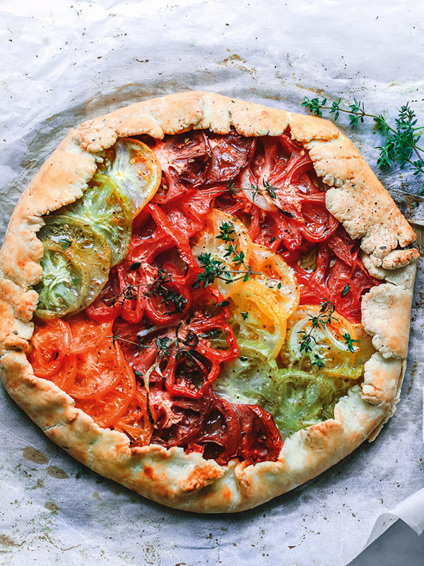 Bunte Tomaten-Tarte mit roten, gelben, grünen, orangefarbenen und schwarzen Tomatenscheiben auf goldbraunem Mürbeteig, dekoriert mit frischem Thymian.