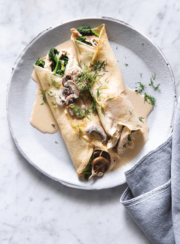 Zwei gefüllte Crêpes mit Hähnchenfleisch, Pilzen, Spinat und cremiger Sauce, angerichtet auf einem hellen Teller und mit frischem Dill bestreut.