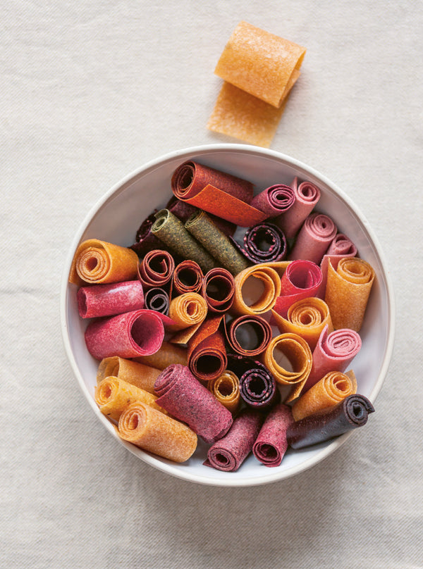 Bunte Fruchtleder-Röllchen aus verschiedenen Früchten in einer weißen Schale – natürlich getrocknet und liebevoll gerollt