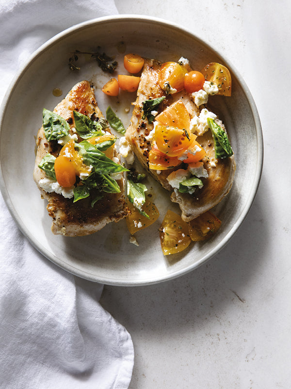 Gegrillte Hähnchenbrust mit frischen Tomatenwürfeln, Basilikum und zerbröckeltem Feta, angerichtet auf einem hellen Teller.