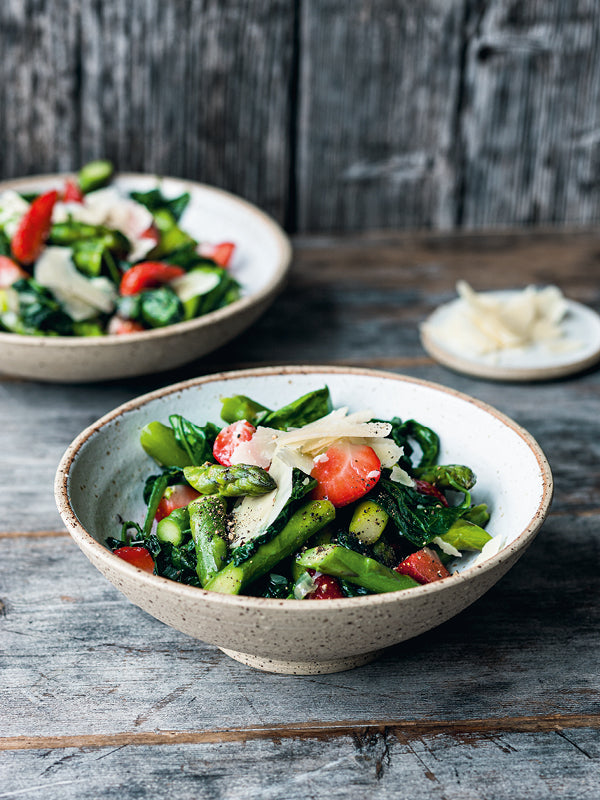 unter Frühlingssalat mit grünem Spargel, Babyspinat, frischen Erdbeeren und gehobeltem Parmesan in einer rustikalen Keramikschale auf Holztisch.