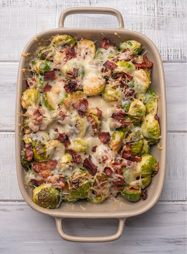 Überbackener Rosenkohl in einer Auflaufform, gemischt mit knusprigem Speck und geschmolzenem Käse, goldbraun gebacken
