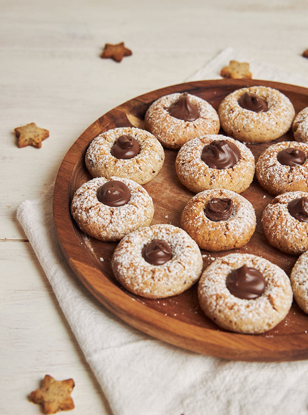 Schoko-Haselnuss-Plätzchen auf Holzteller – mürbe Weihnachtskekse mit Schokoladenfüllung und Puderzucker, perfekt zum Verschenken oder Genießen.