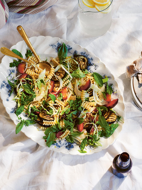 Sommerlicher Nudelsalat mit gegrillter Aubergine, Fenchel, frischen Kräutern und Pflaumen auf weißem Porzellanteller