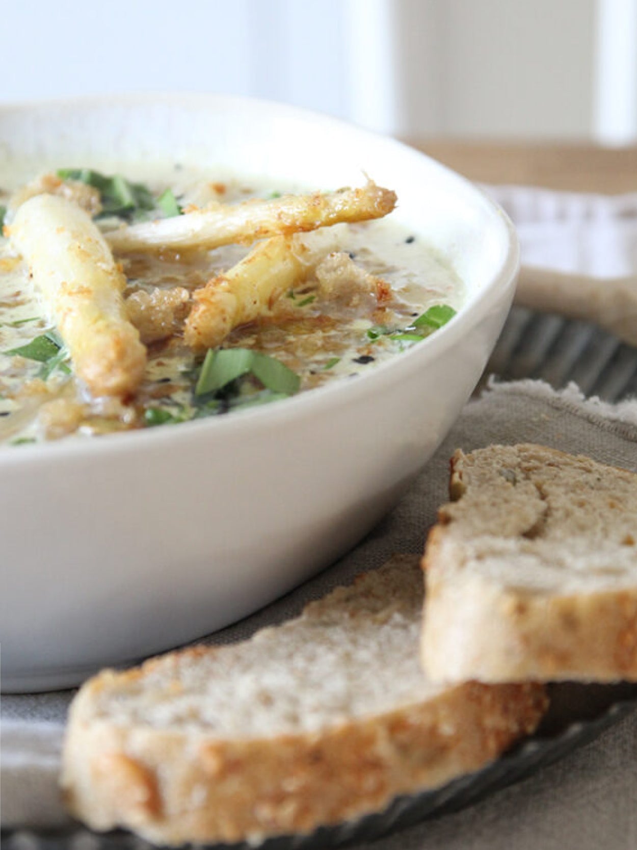 Cremige Spargelsuppe mit angebratenen Spargelstangen und knusprigen Brotbröseln, serviert in einer weißen Schale, dazu frisches Brot.