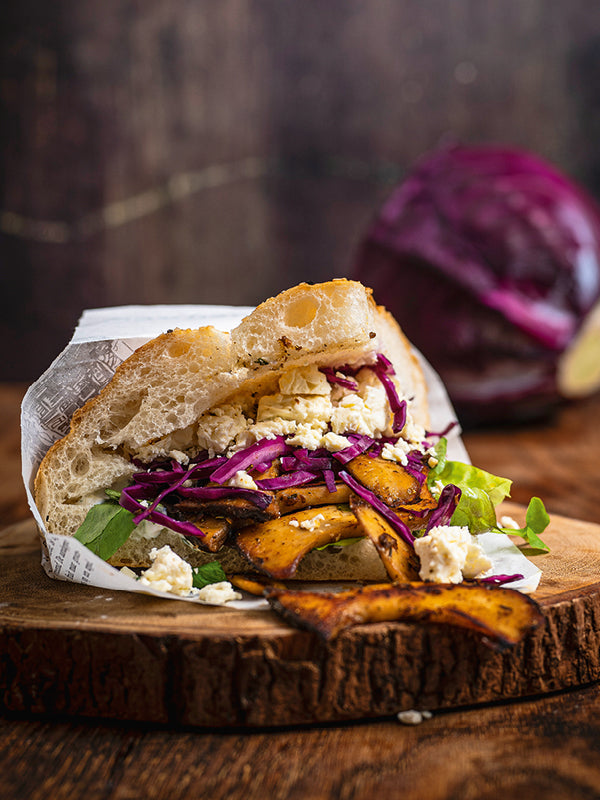Vegetarischer Kebap-Döner mit Kräuterseitlingen, Rotkohlsalat, Joghurtsoße und Feta im Fladenbrot auf rustikalem Holzbrett.