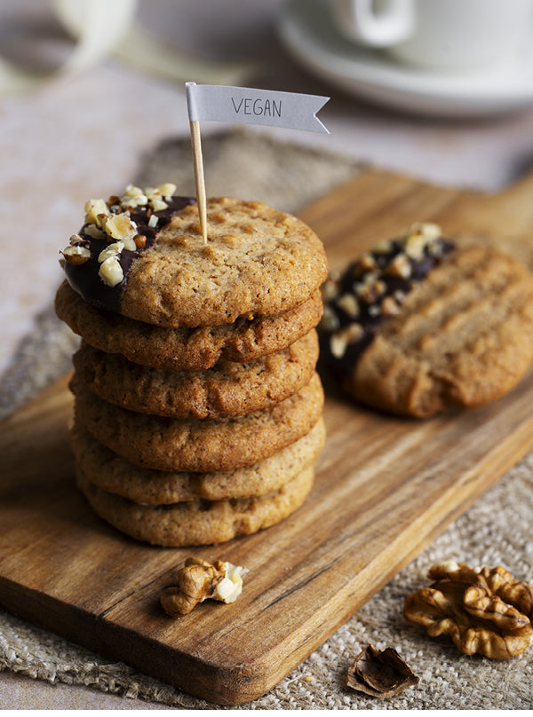 Vegane Walnuss-Schoko-Kekse – goldbraune Kekse auf Holzbrett, teils in Schokolade getaucht und mit gehackten Walnüssen bestreut, im gemütlichen Café-Stil.