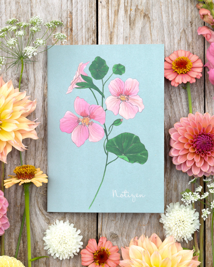 A5 Notizheft Kapuzinerkresse – Gartenzauber Papeterie auf Holztisch, umgeben von bunten Blüten.