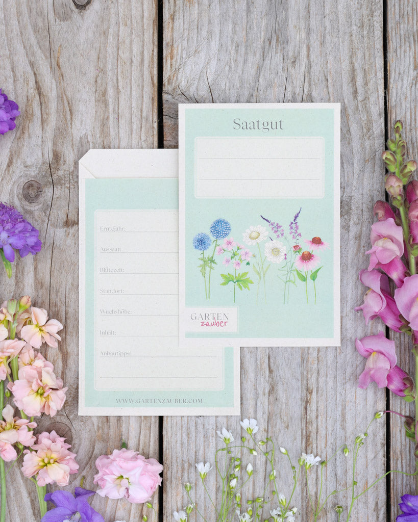 A6 Saatguttüten – Gartenzauber Papeterie, Set mit Vorder- und Rückseite auf Holztisch dekoriert mit Blumen.