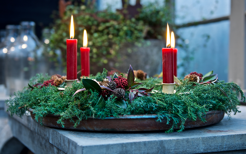 Ein Tablett mit Zweigen und vier roten, brennenden Kerzen.