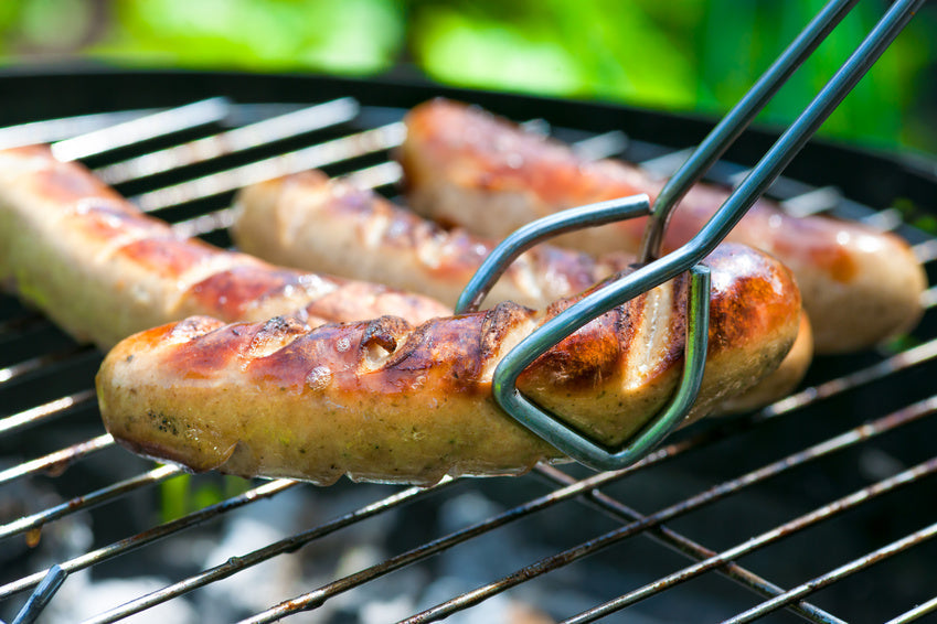 Vier knusprig braune Bratwürtschen liegen auf einem Grillrost.