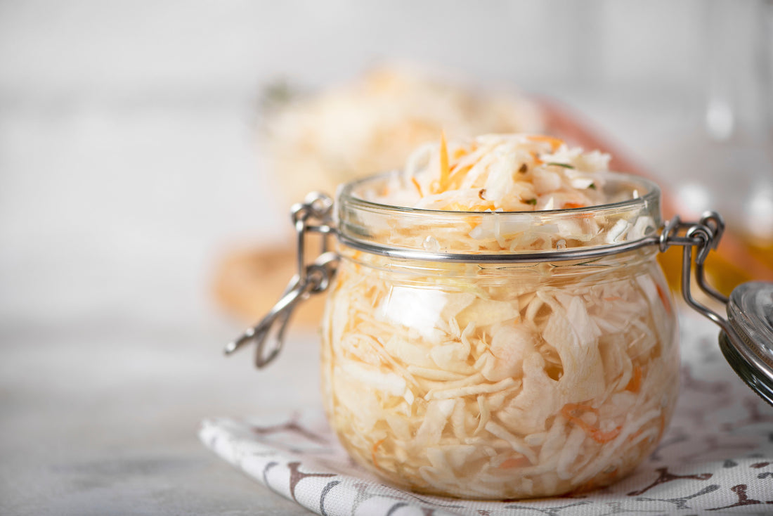 Selbst fermentiertes Sauerkraut in einem Glas mit Bügelverschluss, stehend auf einem Tuch mit dezentem Muster – traditionelle Vorratshaltung mit Weißkohl und Möhren