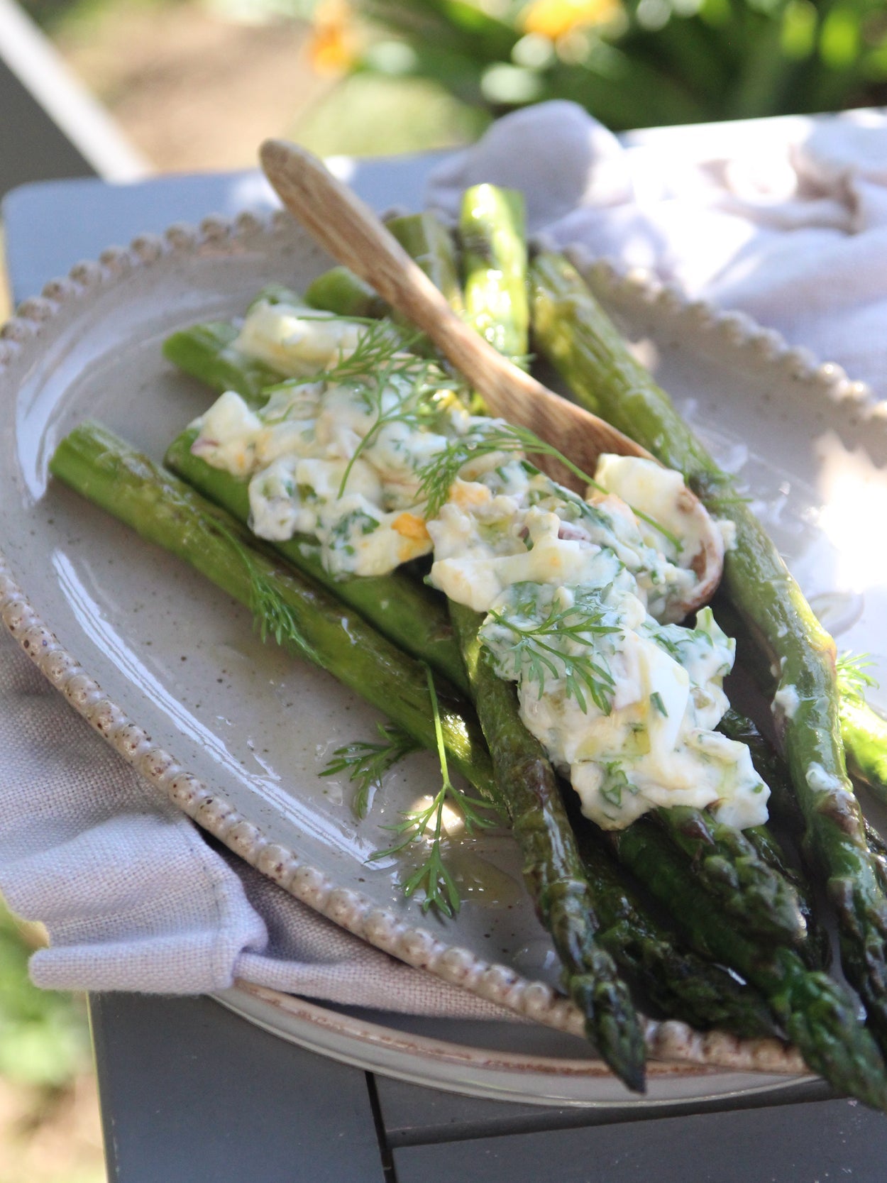 Gebratener grüner Spargel mit cremiger Ei-Radieschen-Vinaigrette, serviert auf einem Keramikteller mit Holzlöffel und frischen Kräutern.