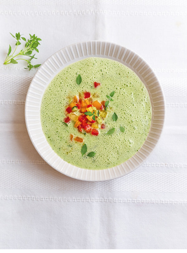 Eisgekühlte Gurken-Joghurt-Suppe in einem hellen Teller, garniert mit bunten Tomatenwürfeln und frischem Basilikum auf weißer Tischdecke.