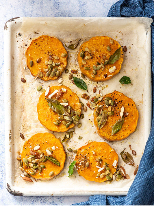 Gerösteter Ofenkürbis mit Kräutern, Kernen und Salzmandeln auf einem Backblech – goldbraun gebacken, aromatisch und herbstlich angerichtet.