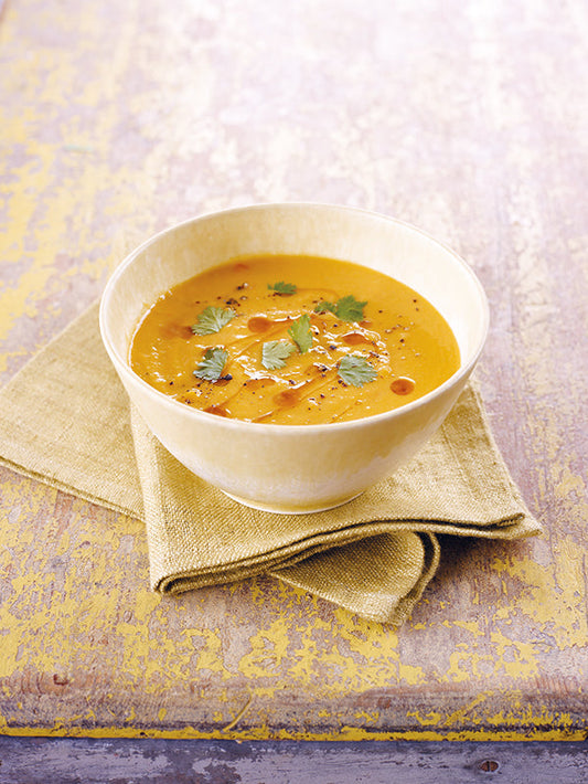 Cremige Kürbissuppe mit Kokosmilch, garniert mit frischem Koriander und Sesamöl, serviert in einer hellen Schale auf einem Leinentuch.