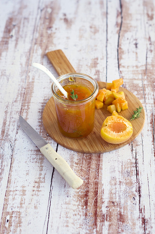 Glas mit selbstgemachter Aprikosen-Thymian-Marmelade auf einem runden Holzbrett