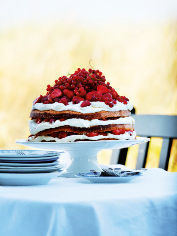 Sommerliche Schichttorte mit frischer Vanillecreme und gemischten Beeren auf einer Tortenplatte im Freien serviert
