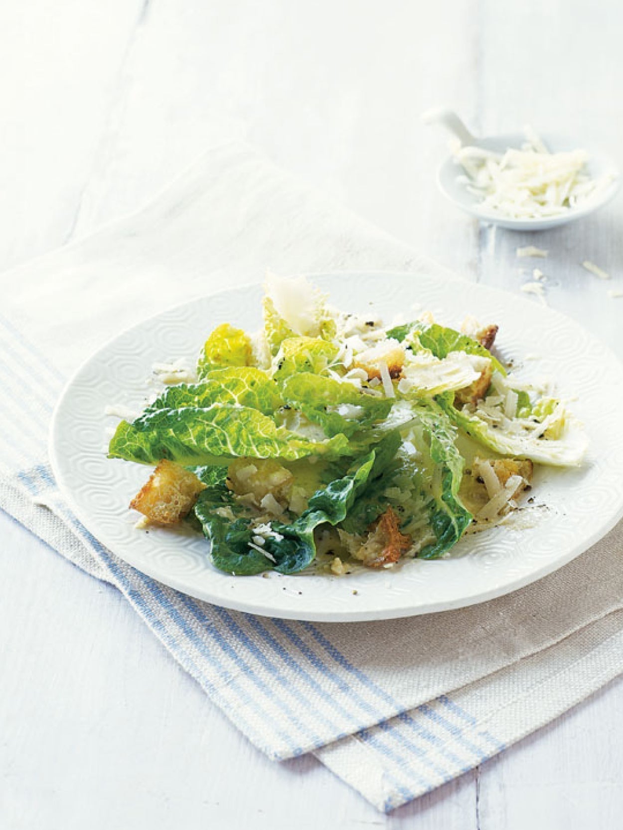 Klassischer Caesar Salad mit Romana-Salat, Croutons und Parmesan auf einem weißen Teller – hell und minimalistisch angerichtet auf Leinentuch.