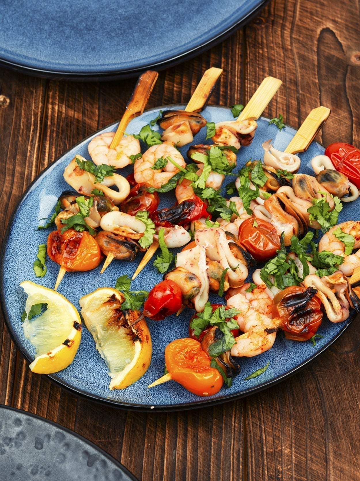Gegrillte Garnelen-Spieße mit Kirschtomaten auf blauer Keramikplatte