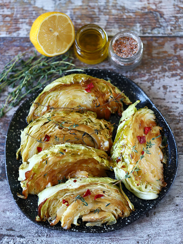 Geröstete Spitzkohl-Steaks auf einem Teller, mit Chili, Thymian und goldbraunen Röstaromen, daneben Zitrone, Olivenöl und Gewürze