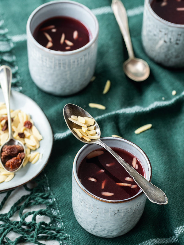 Tasse heißer Glögg mit Sahnehaube, Zimtstange und Schokoladenspänen auf einem Tablett mit Tannenzweig.