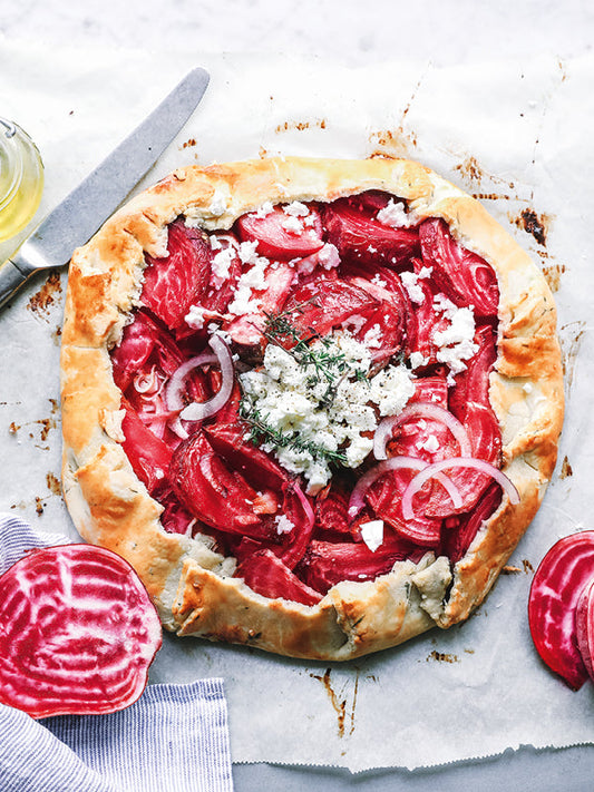 Rustikale Rote-Bete-Tarte mit roten Zwiebeln, Feta und Thymian auf Backpapier, eingerahmt von goldbraunem Mürbeteig.