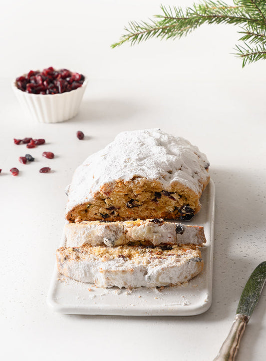 Aufgeschnittener Christstollen mit Marzipankern, Puderzuckerhaube und getrockneten Cranberrys auf einem weißen Teller.