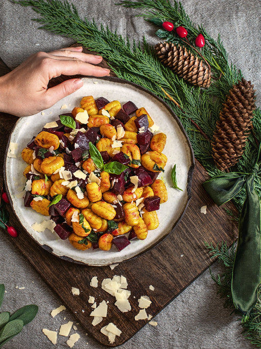 Goldene Kürbisnocken und gewürfelte Rote Bete auf einem Teller, serviert mit frischem Basilikum und Parmesan, arrangiert im winterlich dekorierten Setting.