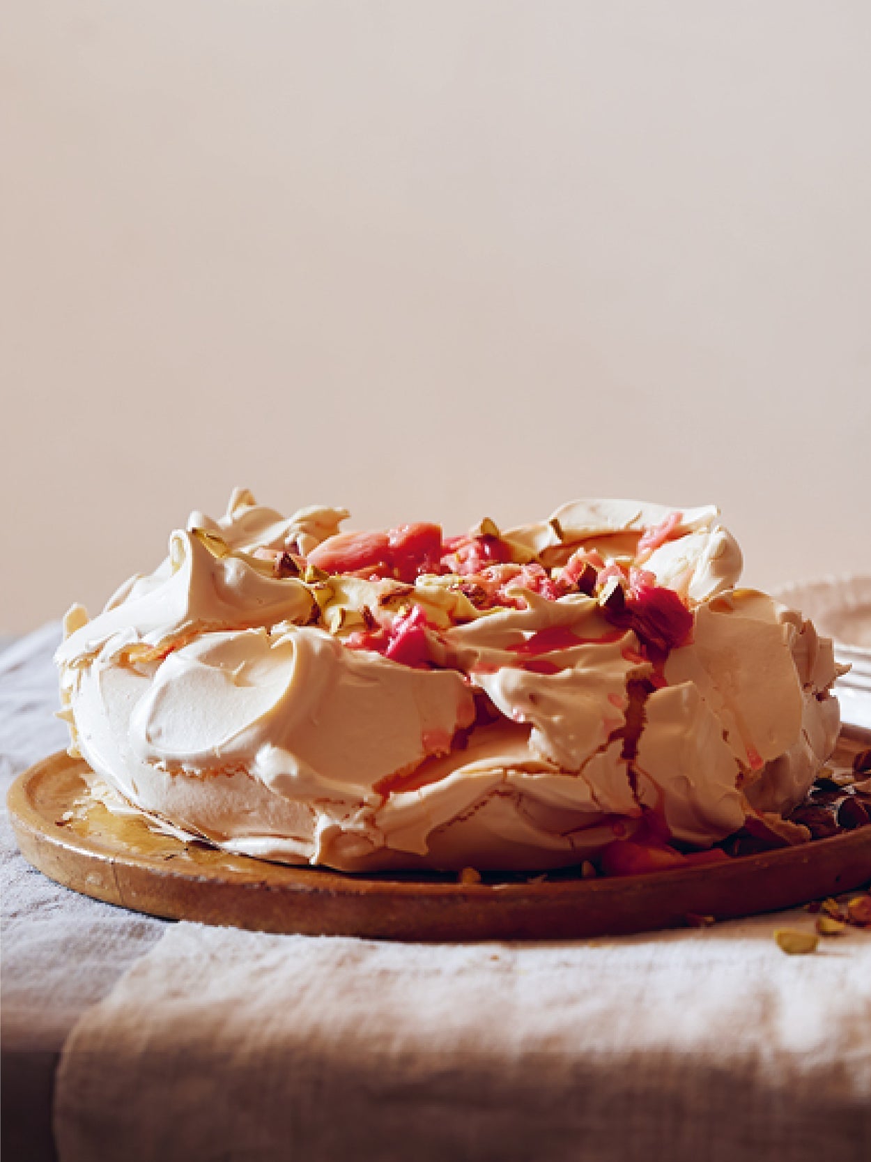 Pavlova mit luftigem Baiser, fruchtigem Rhabarberkompott und gehackten Pistazien auf einem Holzbrett serviert