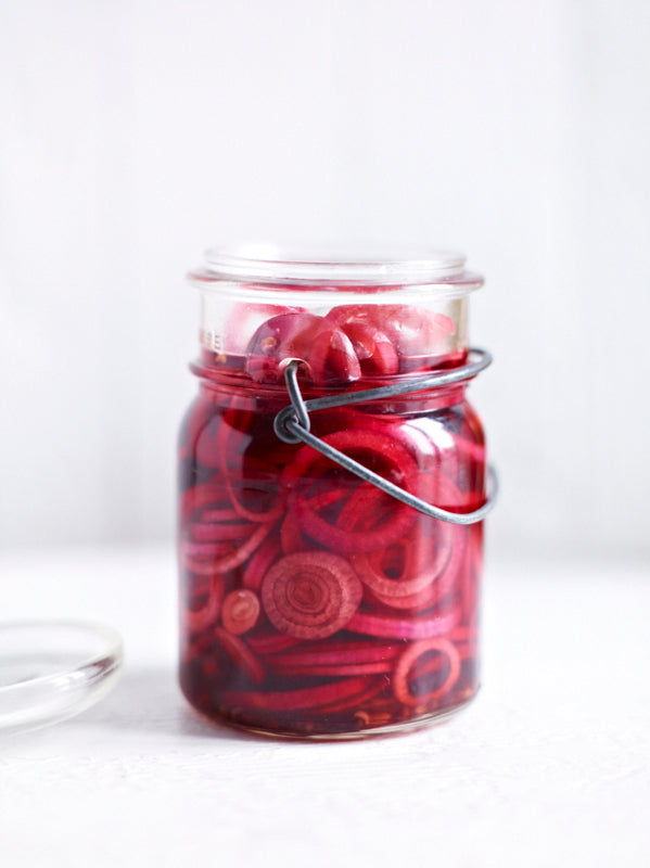 Leuchtend pink eingelegte rote Zwiebelringe in einem kleinen Glas mit Drahtbügel – aromatisch eingelegt mit Essig und Gewürzen