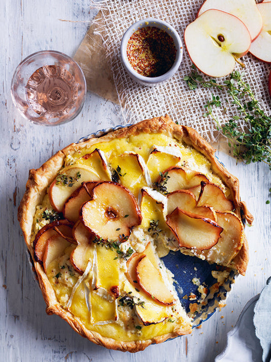 Pikante Apfeltarte mit Brie, Ricotta und Thymian auf rustikalem Untergrund, dekoriert mit Apfelscheiben und Kräutern
