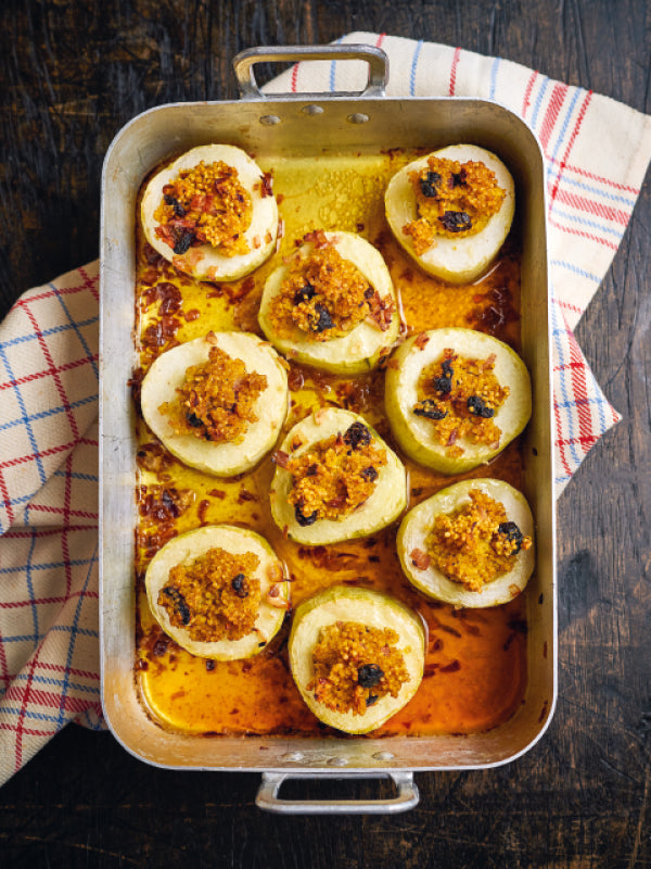 Aufgeschnittene Schmorgurken-Zylinder in einer Ofenform, gefüllt mit würziger Hirse-Sauerkirsch-Mischung, goldbraun geschmort und von aromatischem Sud umgeben.