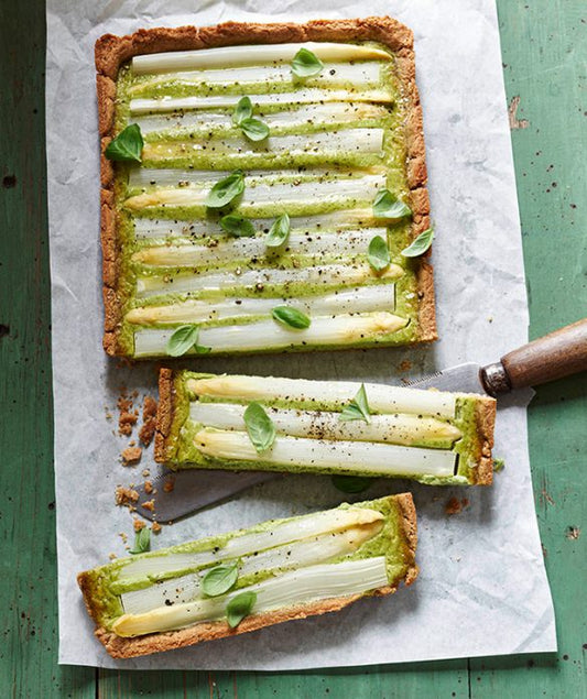 Herzhafte Spargeltarte mit weißem Spargel, Basilikum und goldbraunem Mandelboden – angerichtet auf Backpapier mit Messer.