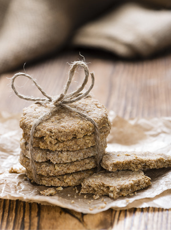 Vegane Haferkekse – goldbraune, knusprige Kekse aus Haferflocken, gestapelt und mit Naturgarn gebunden, auf rustikalem Holz angerichtet.