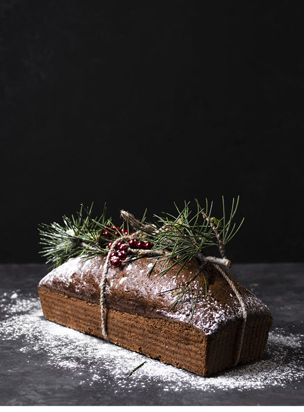 Saftiger Weihnachts-Gewürzkuchen mit Puderzucker, Tannenzweig und roten Beeren – festlich dekoriert und als Geschenk aus der Küche verpackt.