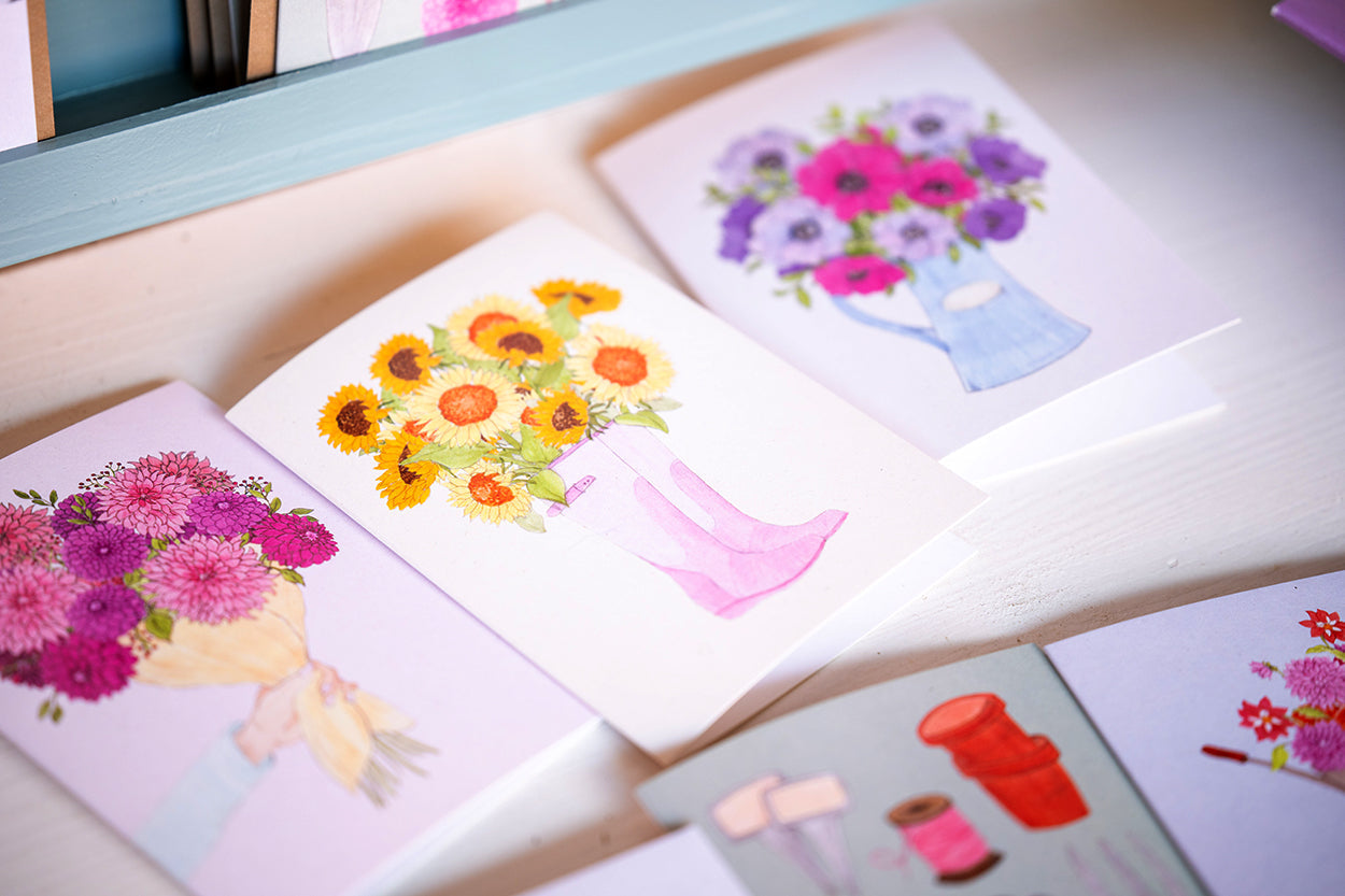 Klappkarten mit einem Strauß in der Hand, Sonnenblumen in pinken Gummistiefeln und einem Krug mit Anemonen.