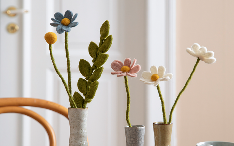 Filzbumen in unterschiedlicher Farbe und Form in Vase auf dem Tisch.
