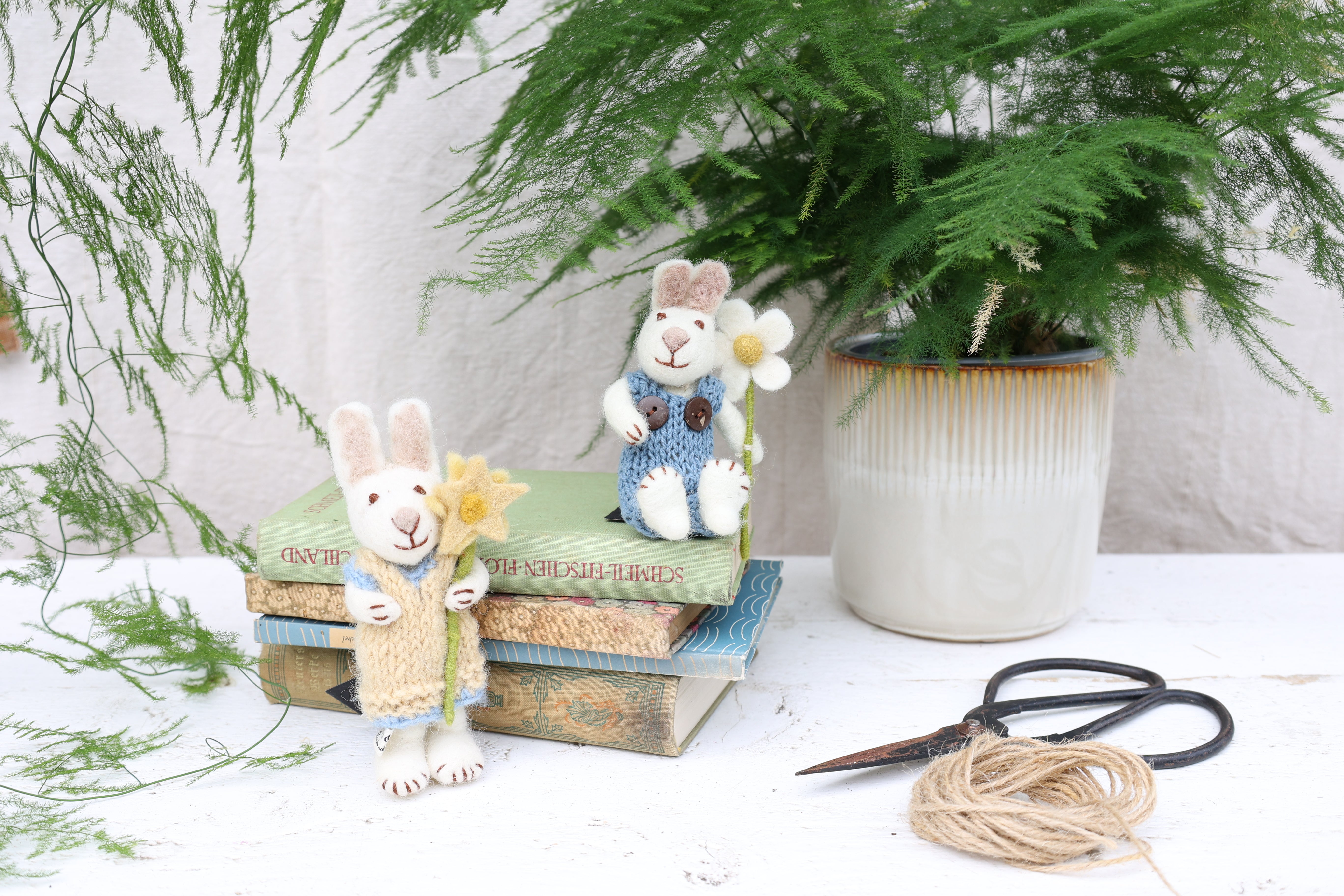 Zwei kleine weiße Filzhäschen mit Blume in der Hand sitzend und stehend, liegende Bücher, Pflanze