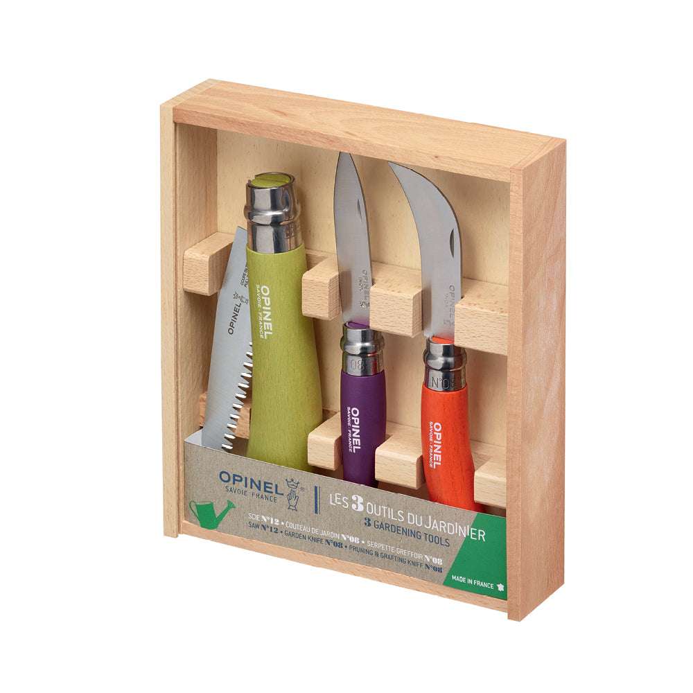 Holzkiste mit Opinel-Gartengeräten: Klappsäge mit grünem Griff, Baumschneidemesser mit lila Griff, Veredelungsmesser mit rotem Griff.