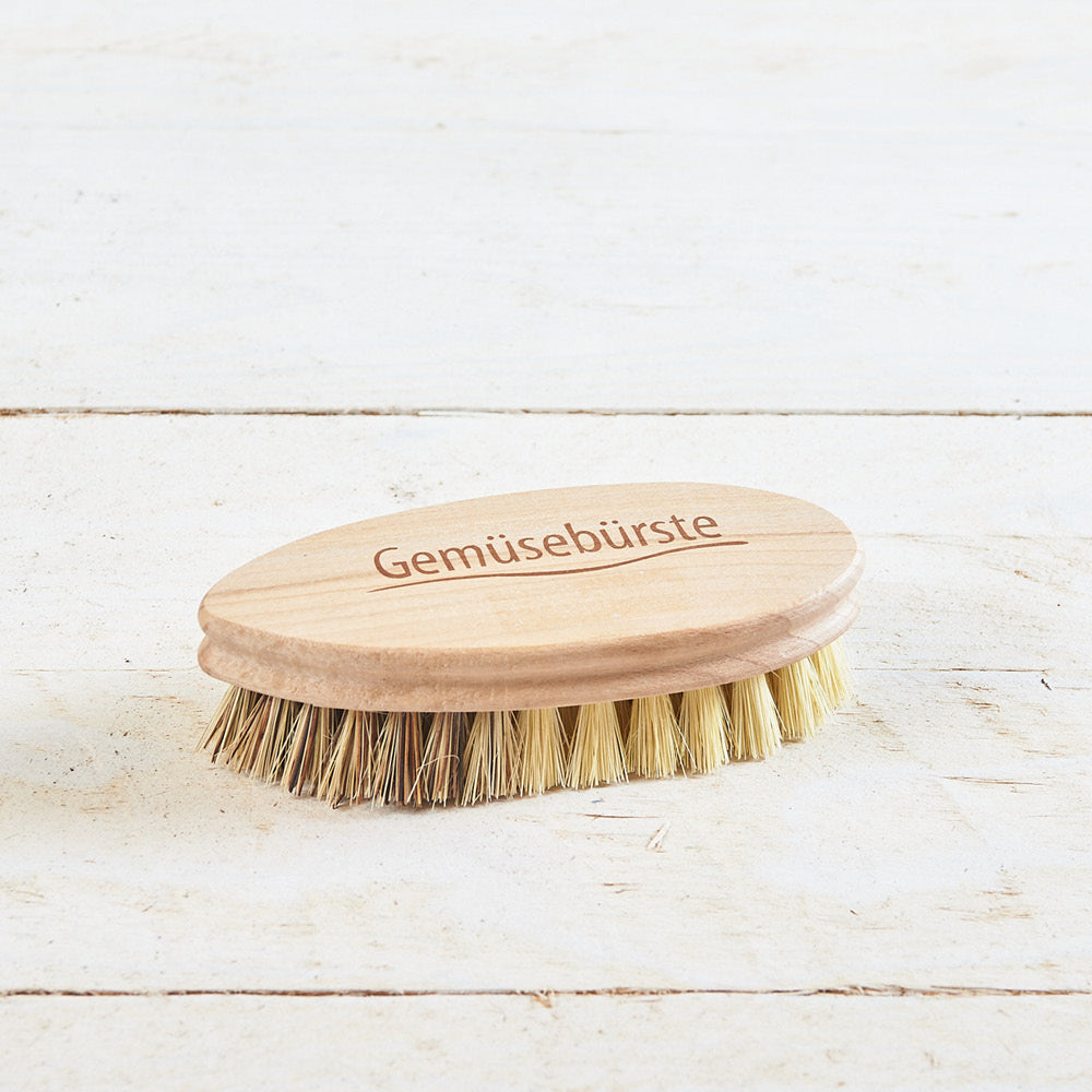 Ovale Gemüsebürste aus Holz mit Naturborsten auf einer hellen Holzoberfläche, oben mit dem Wort „Gemüsebürste“ graviert.