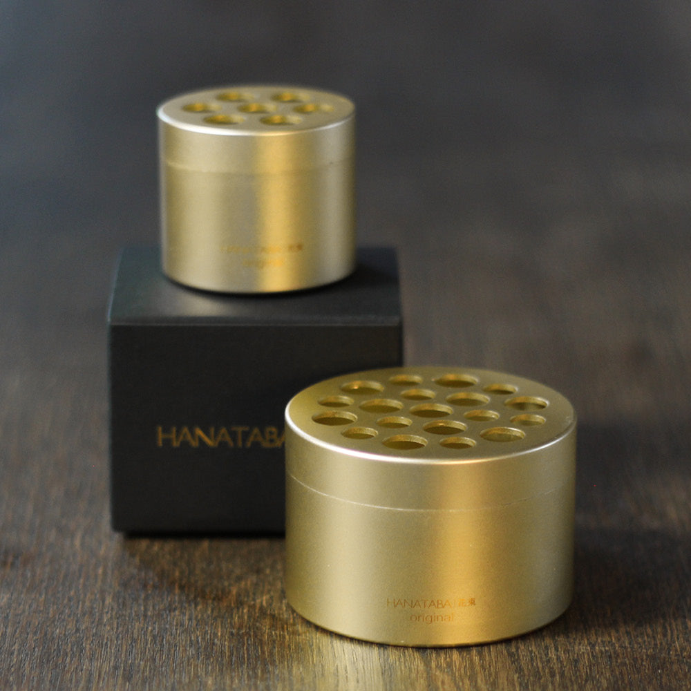 Hanataba in Champagne Gold,  mit edler schwarzer Verpackung auf Holztisch.
