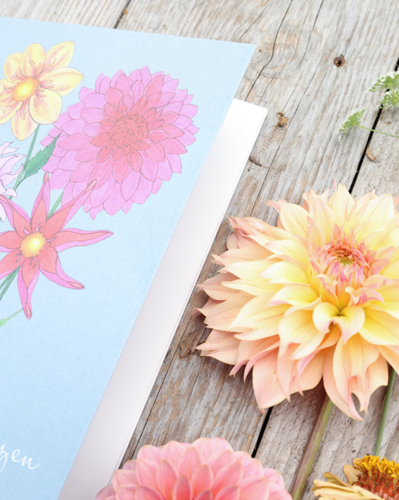 Detailaufnahme des A5 Notizhefts Dahlien – Gartenzauber Papeterie, liegend auf Holztisch mit Dahlienblüten im Hintergrund.
